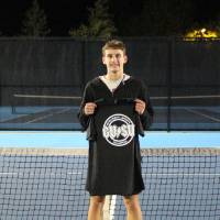 A student holding up championship shirts from a singles tennis tournament